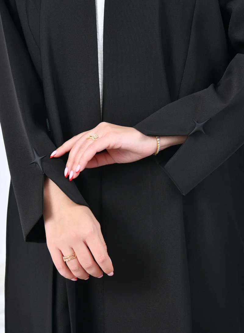 عبايات حوراء عباية سوداء بتصميم انسيابي مميز مزينة بأزرار زينة على شكل نجوم تتميز بقصة ناعمة مع كسرات