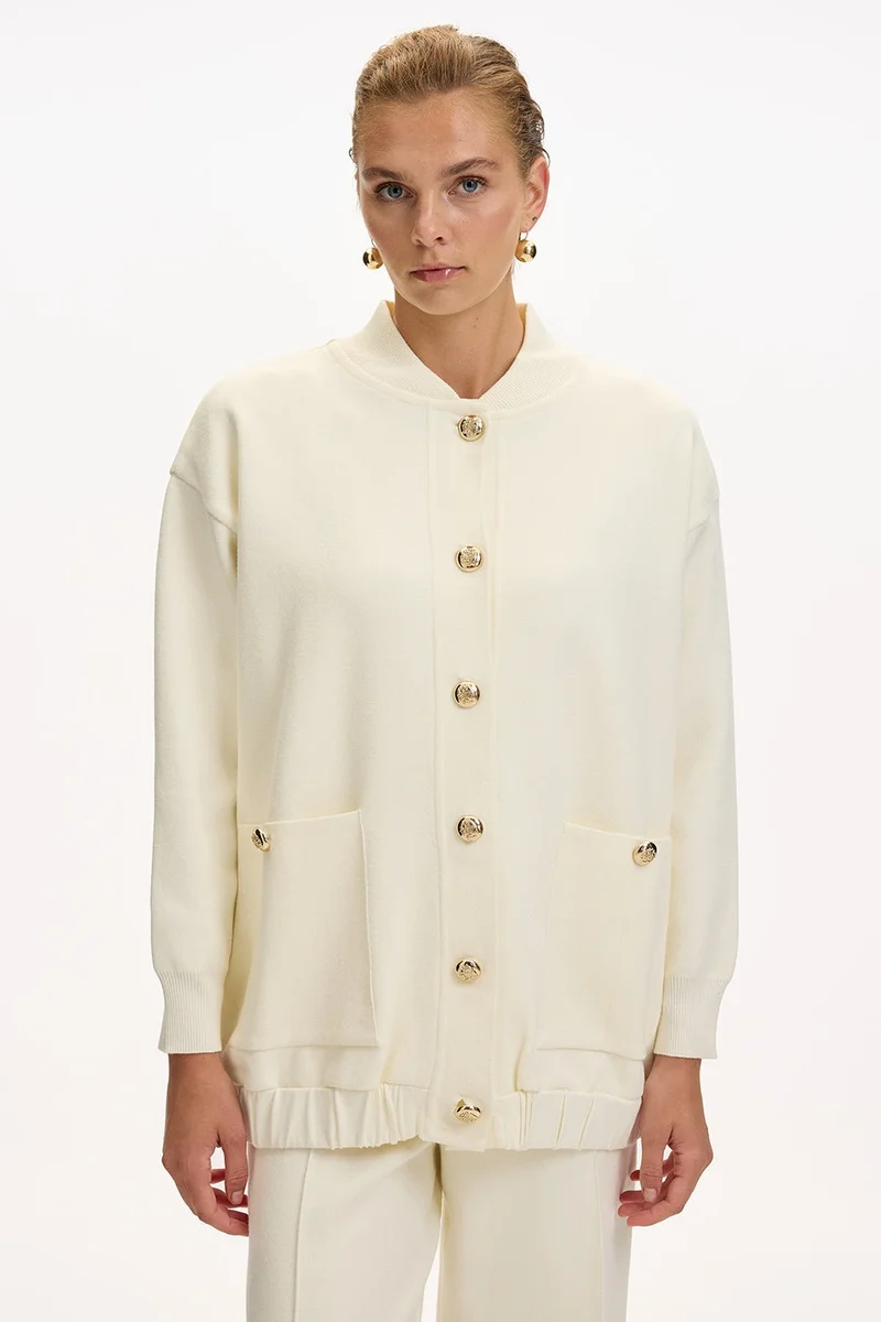 اكسيكيوز كارديجان محبوك بلون بيج فاتح، بياقة دائرية، وجيوب، وأزرار ذهبية، وقصة واسعة.