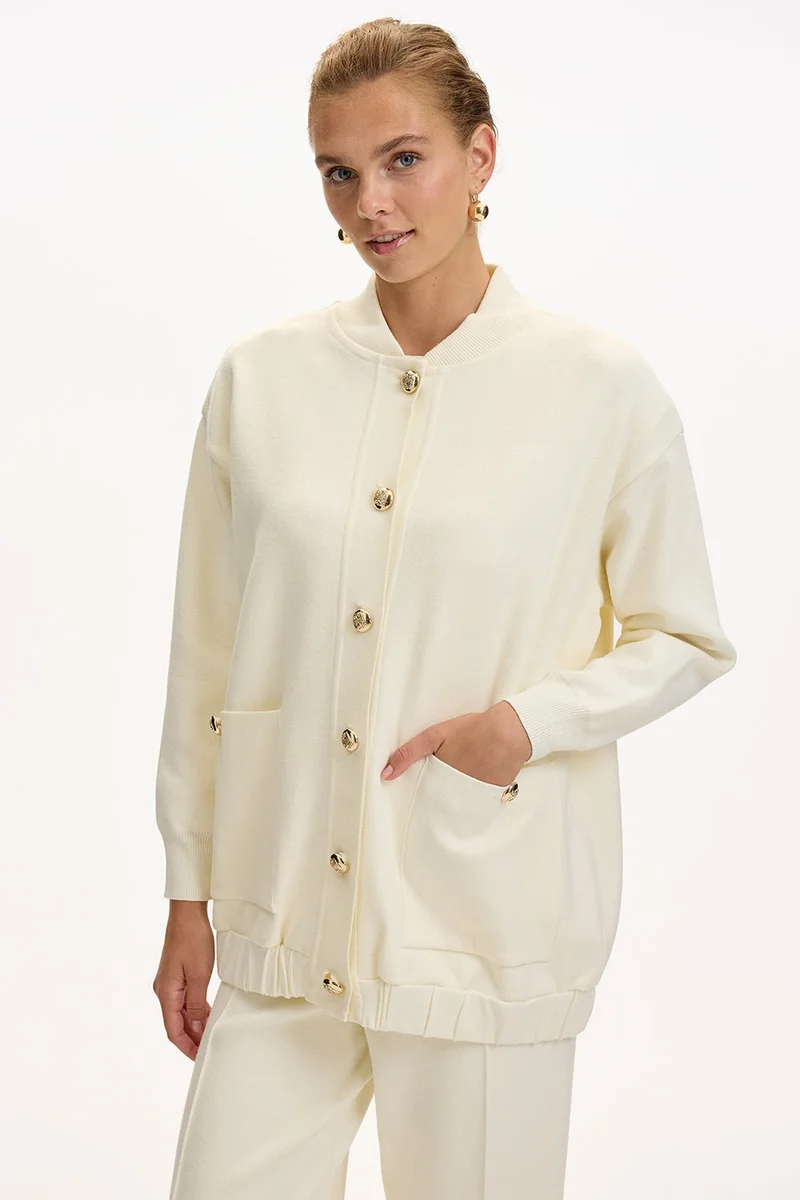 اكسيكيوز كارديجان محبوك بلون بيج فاتح، بياقة دائرية، وجيوب، وأزرار ذهبية، وقصة واسعة.