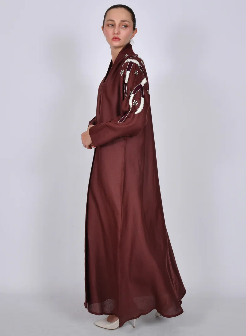 HAWRAA ABAYA A maroon half-cloche abaya decorated with embroidery and prominent beading on the sleeves.