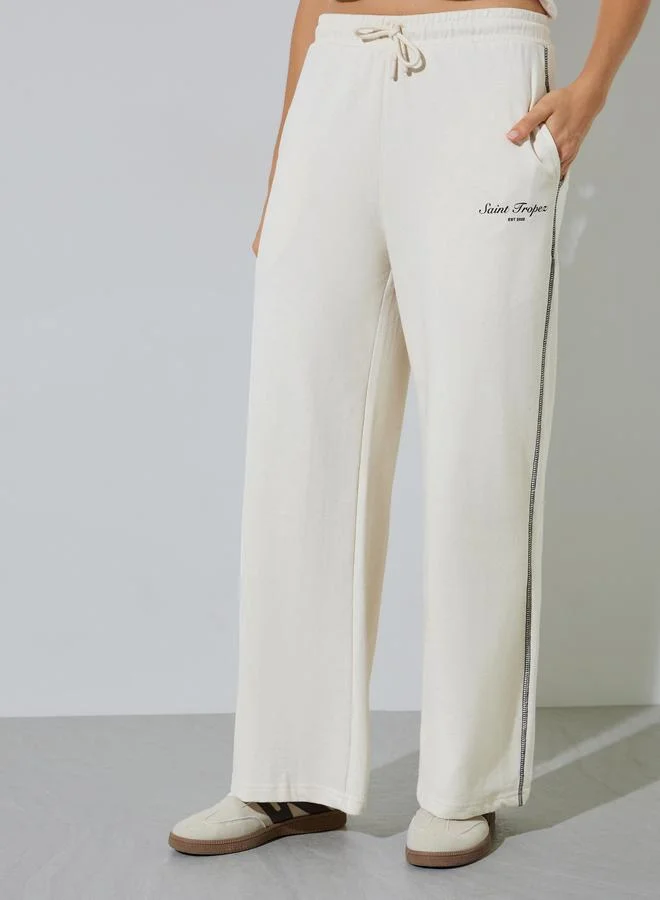 Styli Beige Wide Leg Joggers with Slogan and Cross Stitch Detail
