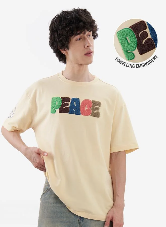 ذا سوليد ستور تيشرت واسع بطبعة جرافيك وتطريز كلمة Peace للرجال - كريمي