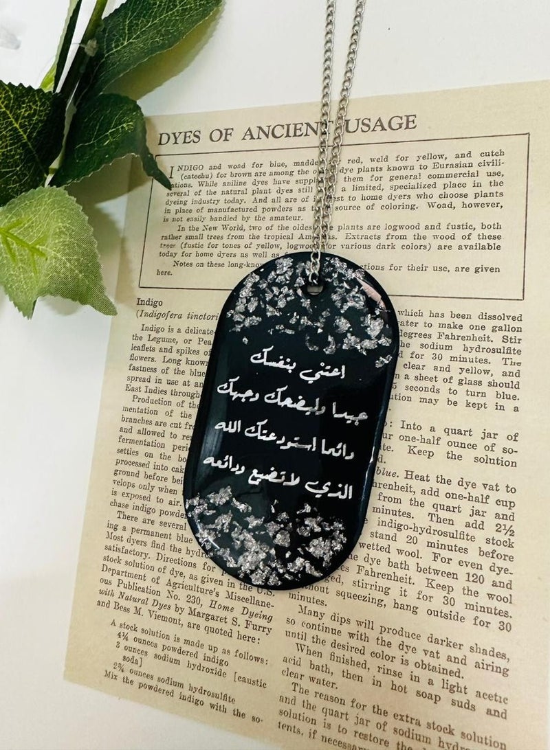 A single face pendant with a phrase in black embroidered with silver leaf made of luxurious resin