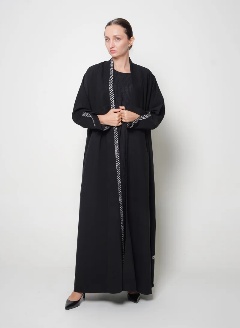 HAWRAA ABAYA Black wrap abaya with a flowing cut and white embroidery.