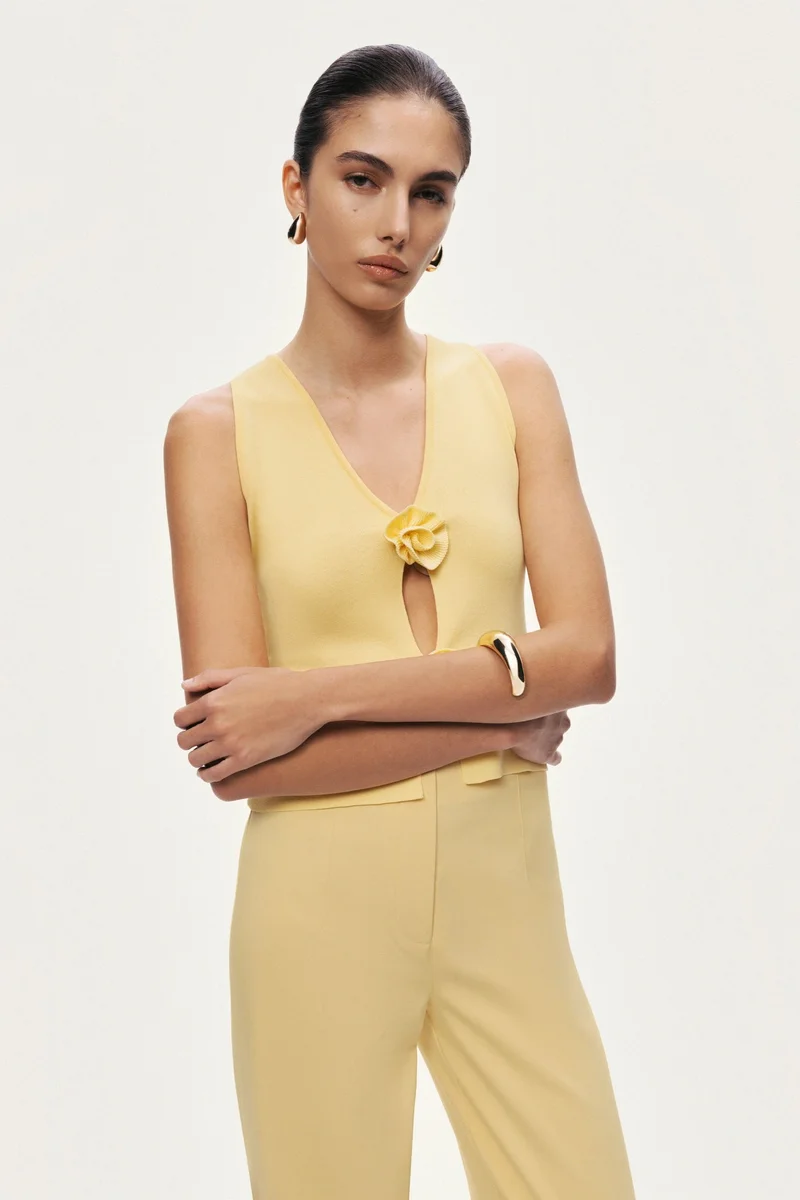 نوكتورن A refined knit top designed with a deep V neckline and subtle cut-out detail, finished with delicate floral accents for a feminine yet modern statement. Sleek and versatile, it transitions effortlessly from daytime elegance to elevated evening styling.– True to size– Slim fit silhouette– Sleeveless design with deep V neckline– Front cut-out detail with floral embellishments– Soft, stretch knit construction-Model is 5'11" (180 cm) tall with a 32.5" bust, 24.5" waist, and 36" hips, wearing a size S