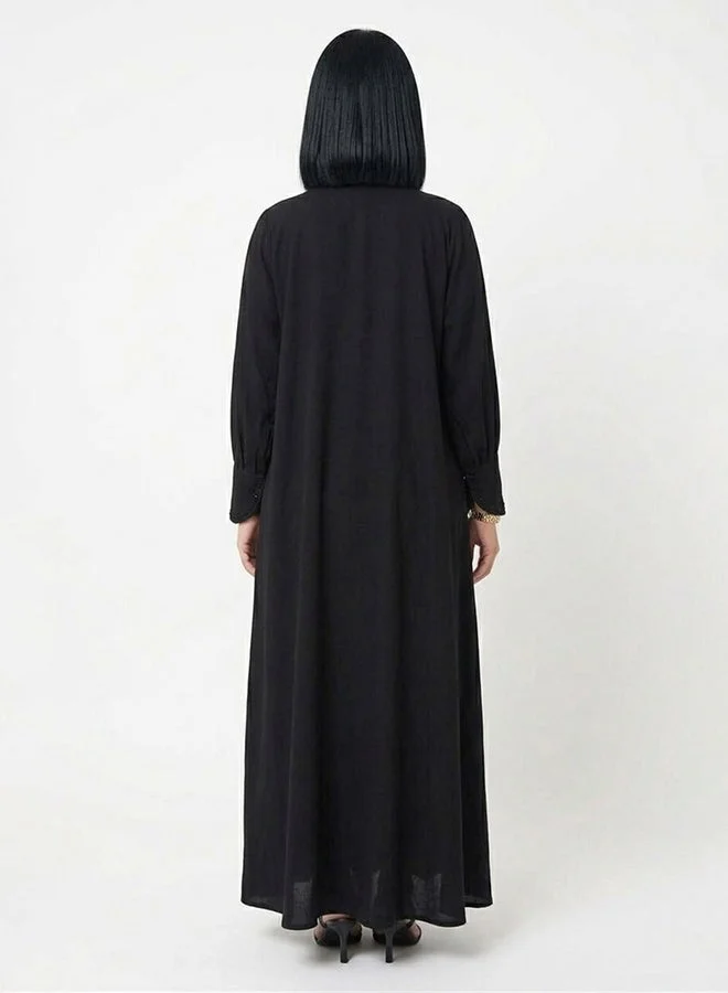 HAWRAA ABAYA Black closed abaya with snap-button closure, adorned with embellishments and embroidery, featuring bell sleeves