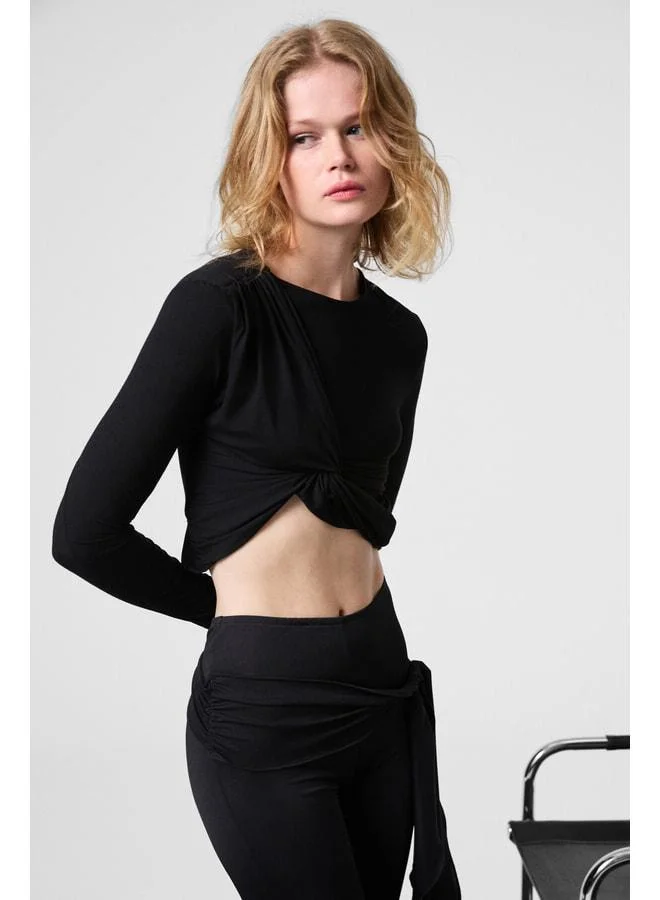 GRIMELANGE SLATE Women's round‑neck crop black blouse with front knot detail and body‑hugging stretch fabric.