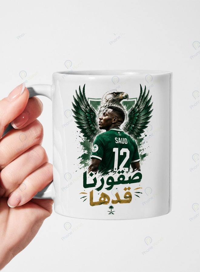 كوب من السيراميك الأبيض يحمل تصميمًا لنجم المنتخب السعودي سعود عبد الحميد مع عبارة صقورنا قدها