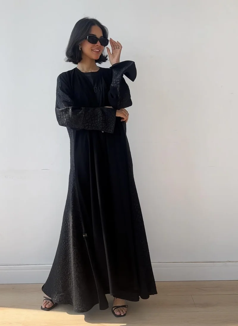 عبايات لوسين Make your day special with this elegant black cloché abaya crafted from luxurious fabric, featuring sophisticated jacquard detailing on the back for a unique and striking look.