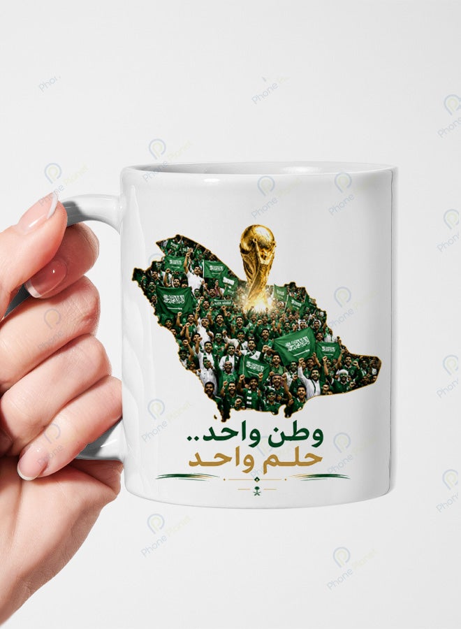 كوب من السيراميك الأبيض يحمل تصميمًا للمنتخب السعودي مع عبارة وطن واحد حلم واحد