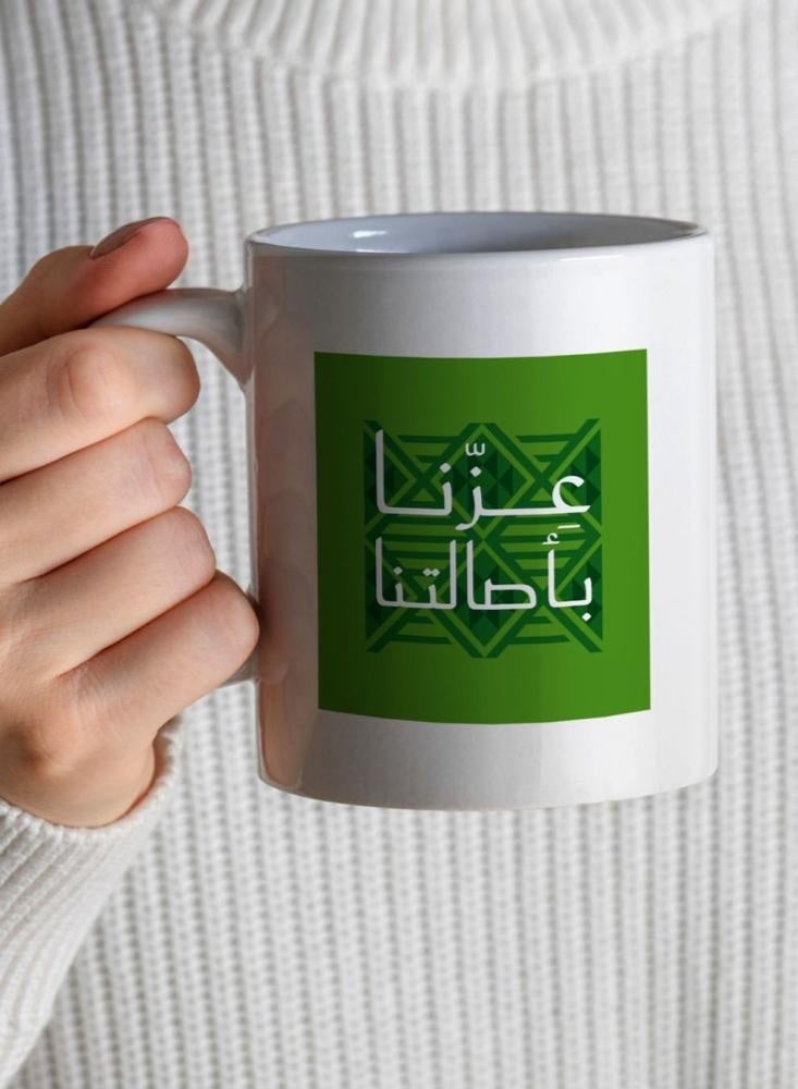 حكاية شمعة اليوم الوطني ، مج من السيراميك بطبعة تصميم "عزنا بأصالتنا" بلون أبيض - Image 1