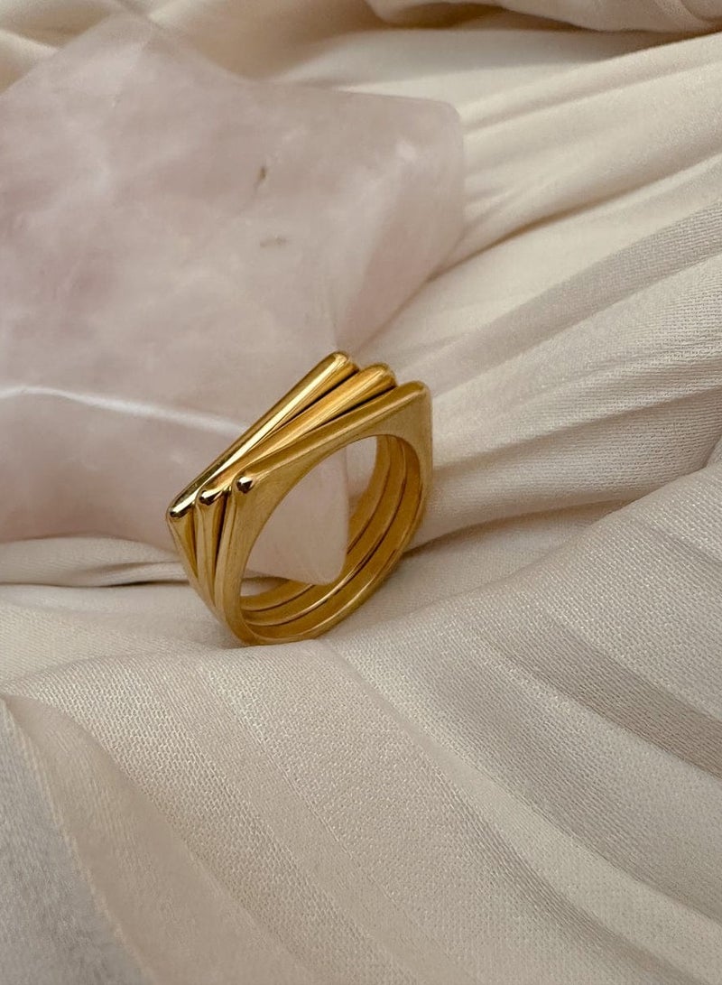 Luxuria A gold ring with a simple geometric design, consisting of three parallel and connected bands, gives it a modern, architectural look. This type of design is often known as a "tri-band ring" or a "layered geometric ring." - Image 1