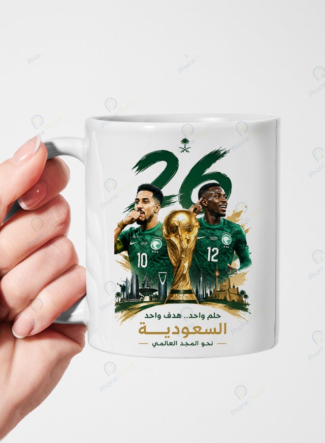 كوب من السيراميك الأبيض يحمل تصميمًا لنجم المنتخب السعودي سعود عبد الحميد وسالم الدوسري مع عبارة حلم واحد هدف واحد