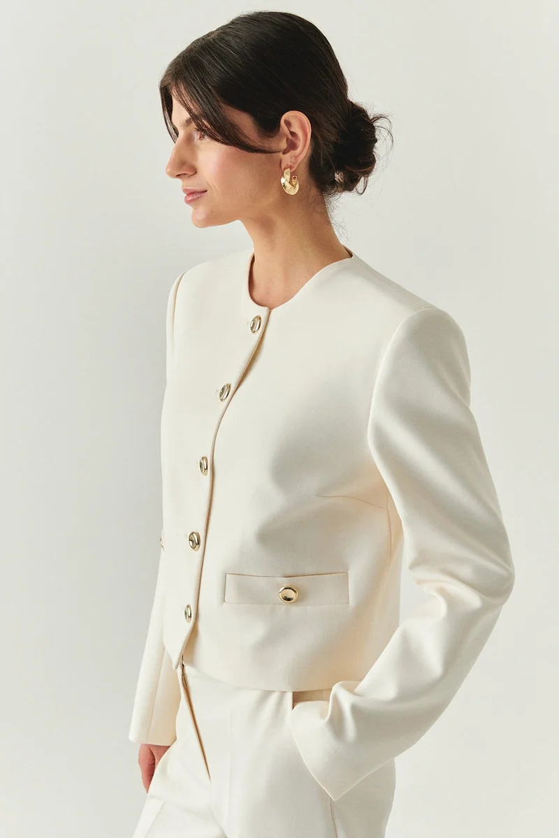 اكسيكيوز جاكيت كريمي اللون بأكمام طويلة وخصر عادي قصير، مزود بوسادات كتف مبطنة وأزرار ذهبية.