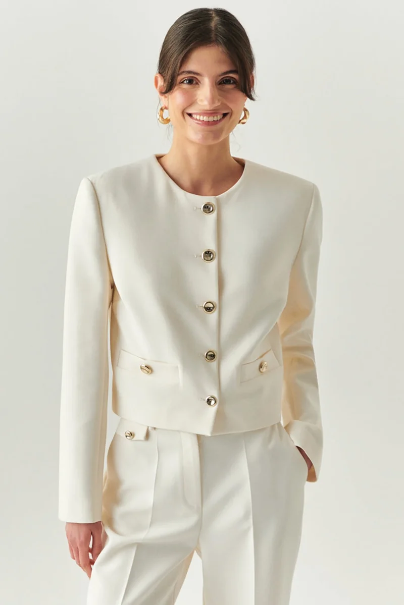 اكسيكيوز جاكيت كريمي اللون بأكمام طويلة وخصر عادي قصير، مزود بوسادات كتف مبطنة وأزرار ذهبية.