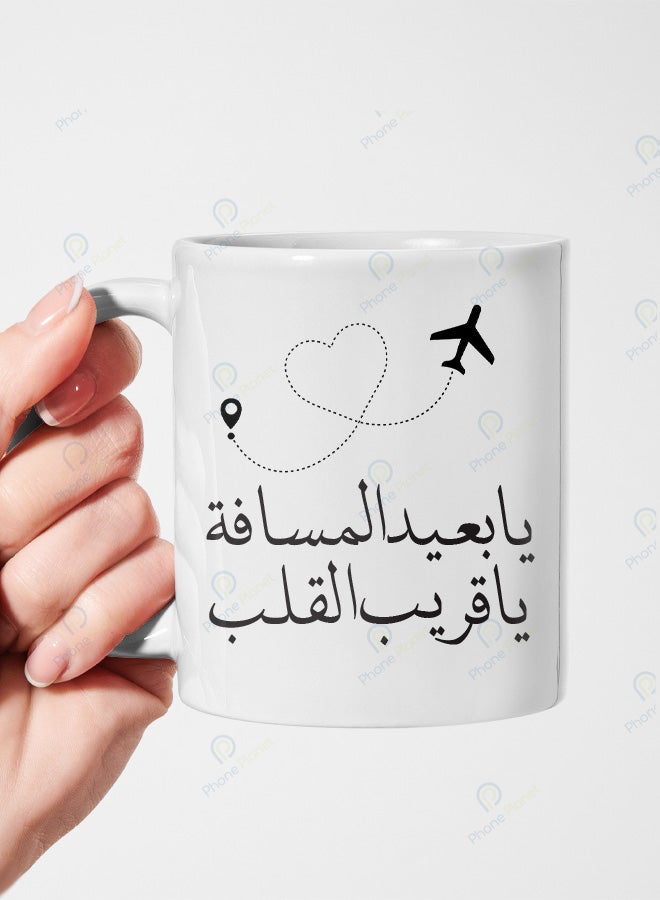 كوب من السيراميك مطبوع عليه عبارة يا بعيد المسافة يا قريب القلب ويتميز بمقبض مريح