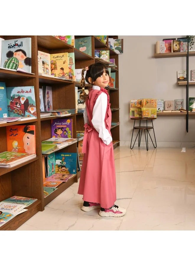 HAWRAA ABAYA Pink apron with long sleeves, ruffles on the shoulders, a zipper closure on the front, pleats at the bottom, and a tightening tie