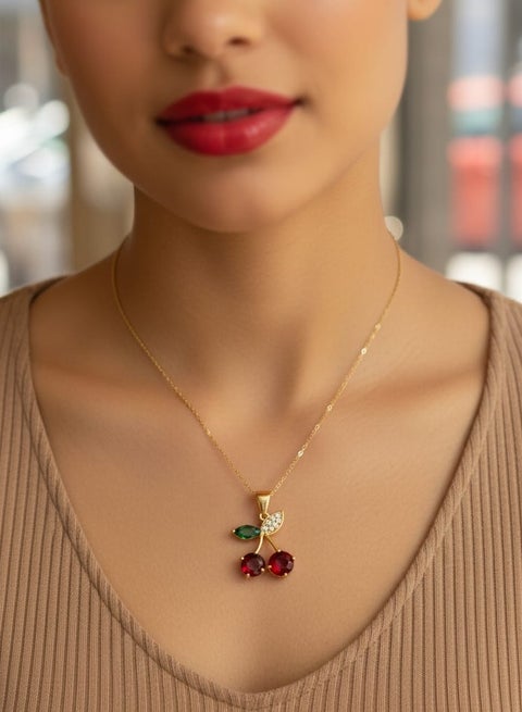 A delicate necklace with a gold-plated chain, featuring a red cherry pendant and sparkling stones - with small, bright green leaves - adjustable to fit your preferred length.