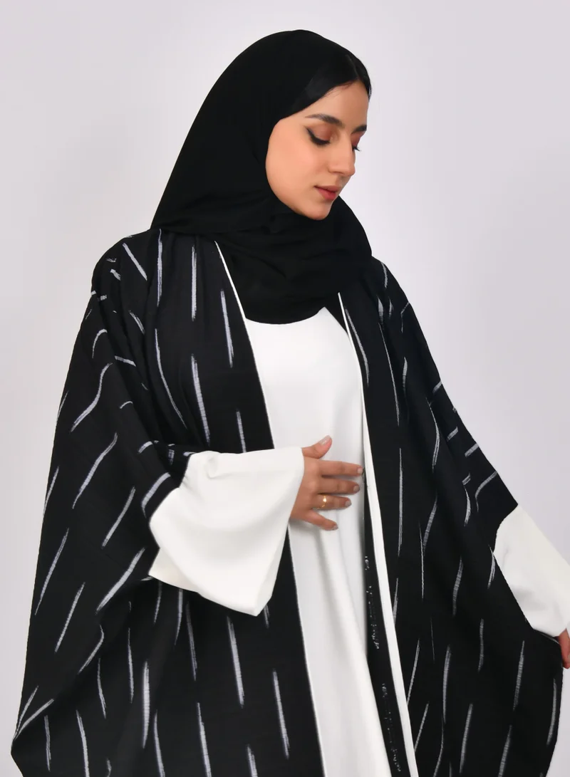 HAWRAA ABAYA Black abaya with wide sleeves and white stripes with a white dress