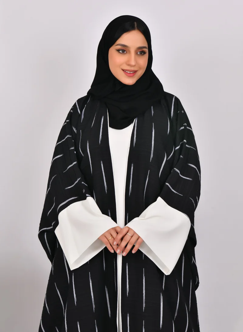 HAWRAA ABAYA Black abaya with wide sleeves and white stripes with a white dress