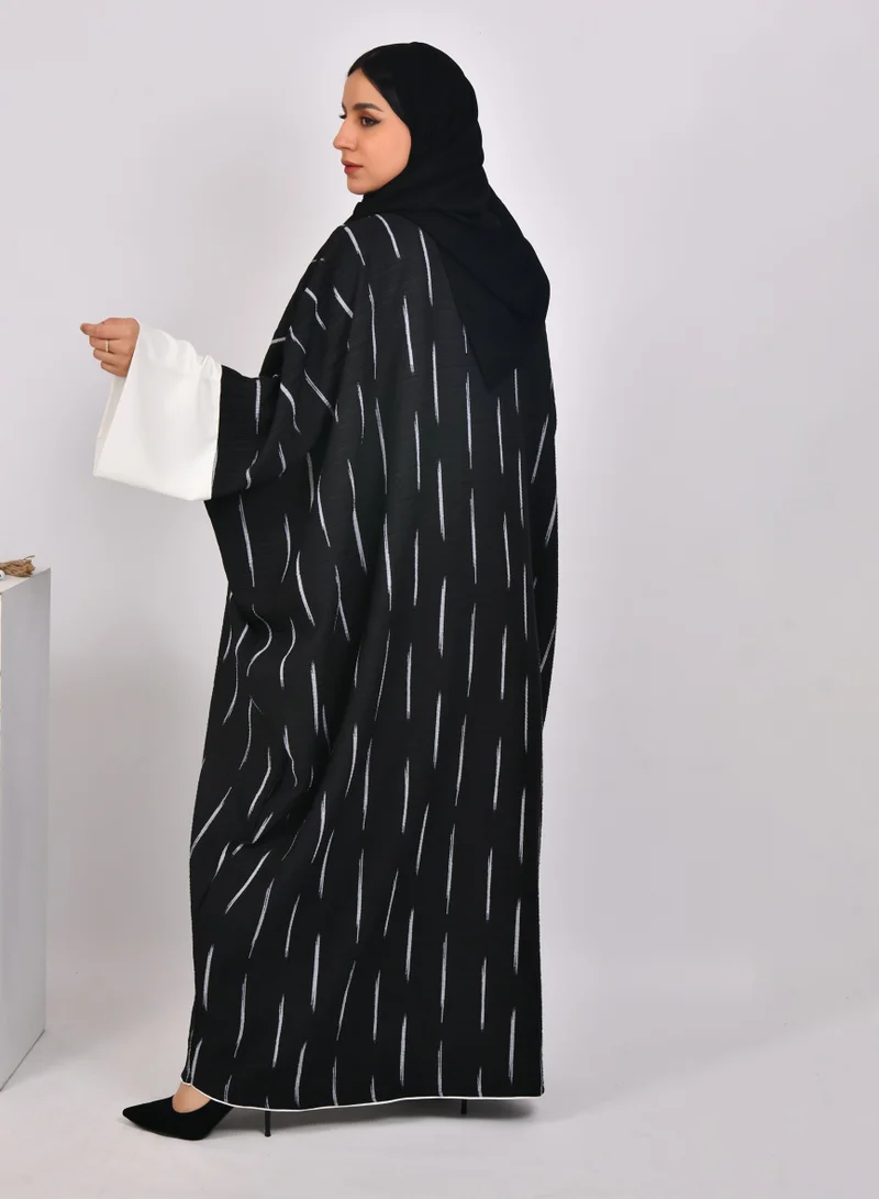 HAWRAA ABAYA Black abaya with wide sleeves and white stripes with a white dress