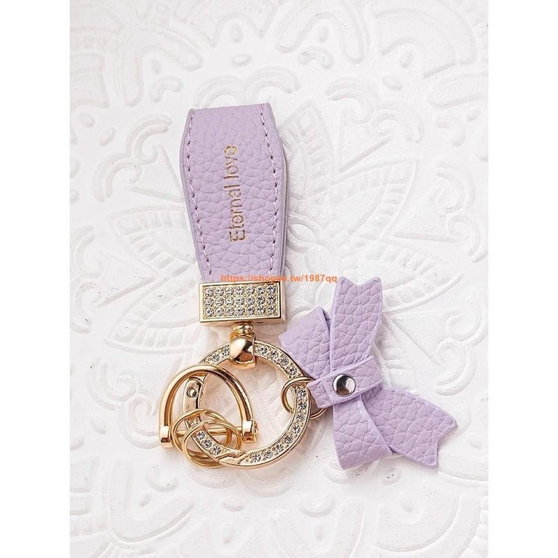 Purple and gold keychain decorated with a faux leather strap, bow, metal frame with shiny stones