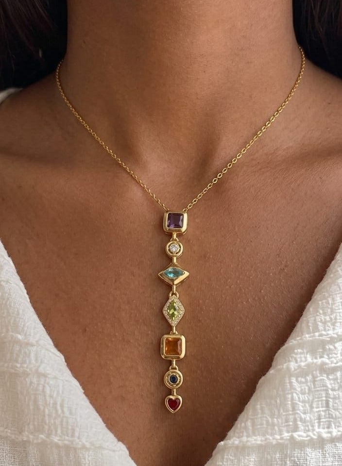 Luxuria An elegant gold-plated pendant necklace, featuring a longitudinal design studded with seven gemstones of various shapes and colors, arranged vertically to end with a small red heart-shaped pendant. - Image 2
