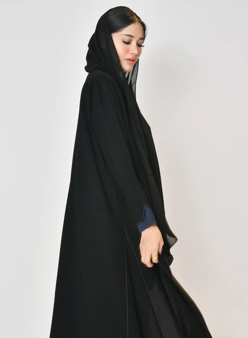 HAWRAA ABAYA Black wrap abaya with quarter-cloth fabric, puff sleeves, and navy color overlapping on the sleeves and the front and side edges of the abaya in an arrow shape