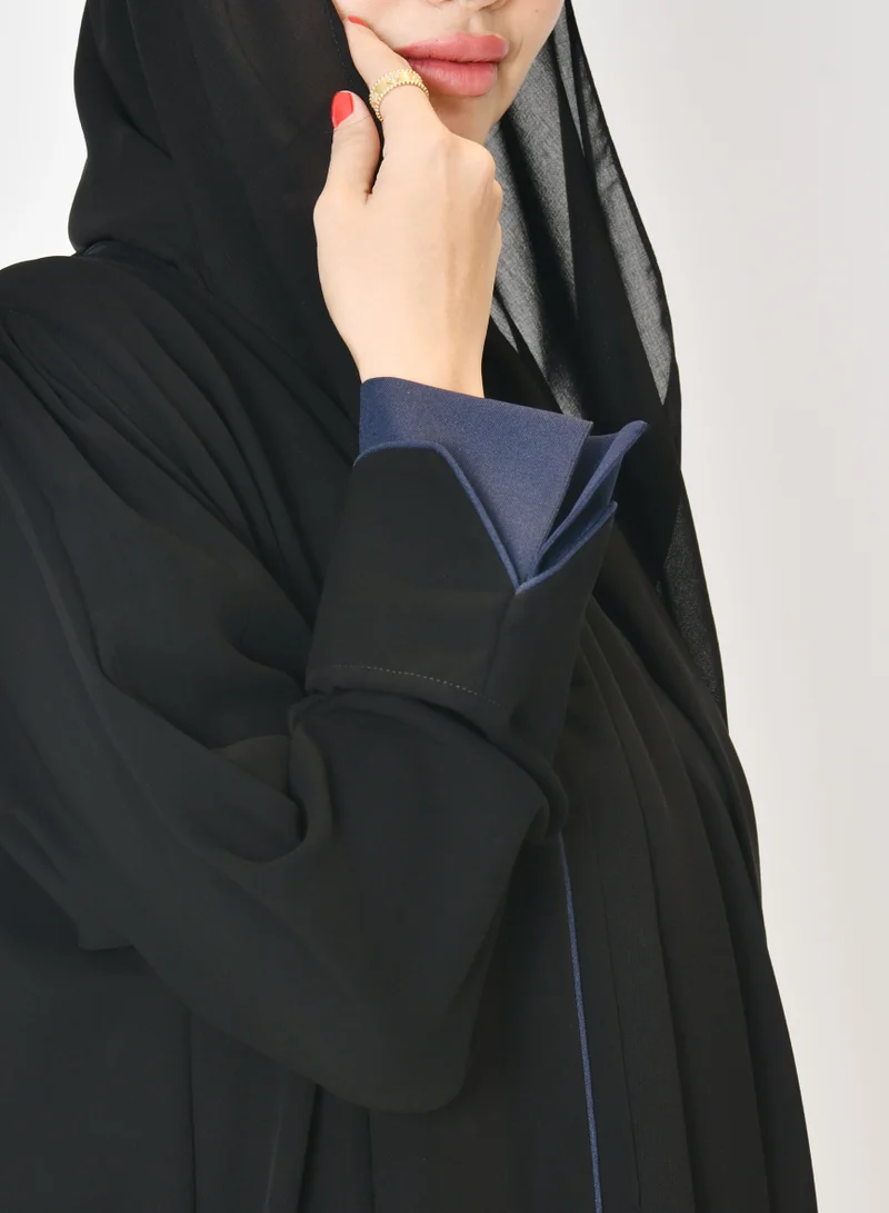 HAWRAA ABAYA Black wrap abaya with quarter-cloth fabric, puff sleeves, and navy color overlapping on the sleeves and the front and side edges of the abaya in an arrow shape