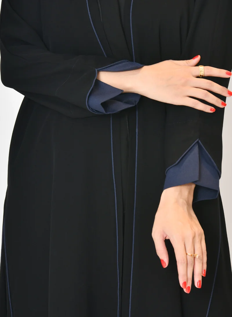 HAWRAA ABAYA Black wrap abaya with quarter-cloth fabric, puff sleeves, and navy color overlapping on the sleeves and the front and side edges of the abaya in an arrow shape