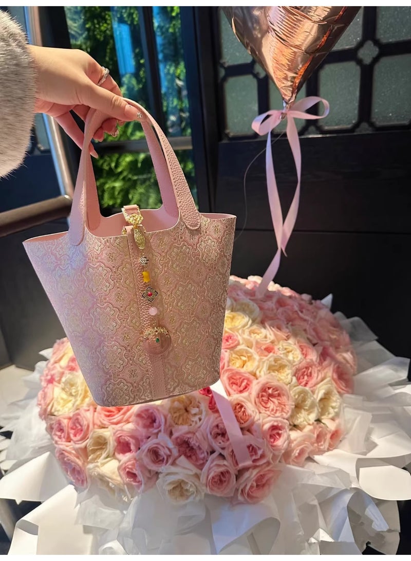 كيفية حقيبة دلو أنيقة بلون وردي فاتح، تتميز بقماش ناعم، وتفاصيل زهور ذهبية، وسحر زخرفي. مثالية للاستخدام اليومي أو المناسبات الخاصة، وتضفي لمسة من الرقي والأناقة على أي إطلالة. - Image 3