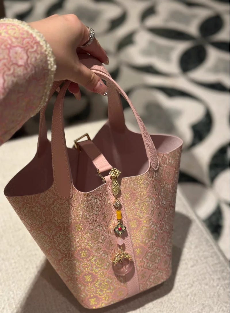 كيفية حقيبة دلو أنيقة بلون وردي فاتح، تتميز بقماش ناعم، وتفاصيل زهور ذهبية، وسحر زخرفي. مثالية للاستخدام اليومي أو المناسبات الخاصة، وتضفي لمسة من الرقي والأناقة على أي إطلالة. - Image 4
