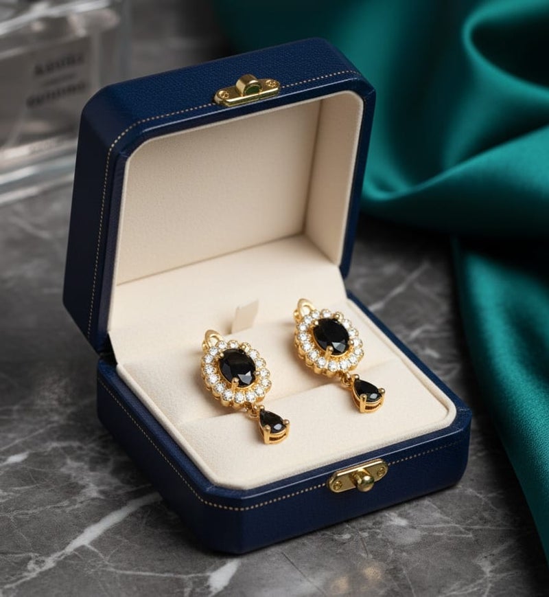 A delicate gold-plated earring featuring a golden flower design studded with shiny stones, a luxurious black stone in the middle, and a luxurious black teardrop stone hanging from it. - Image 1