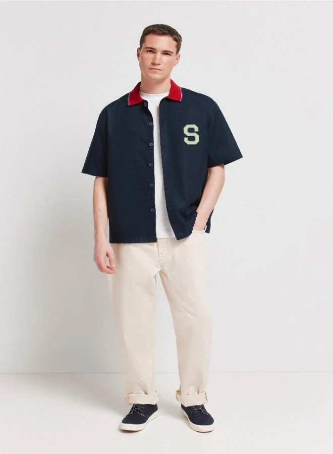 1% cotton oxford boxy fit short sleeve shirt with a ribbed polo collar with stripes, letter patches with embroidery on the back and chest, and a tonal button.
