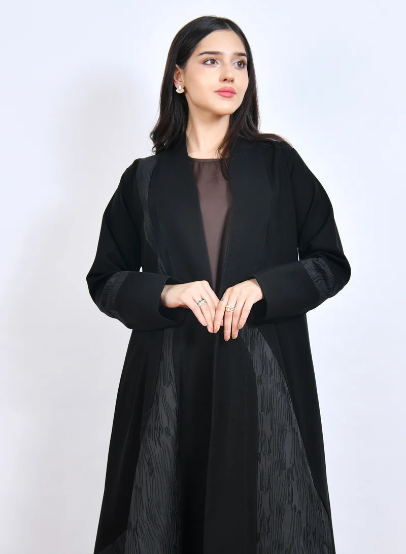 HAWRAA ABAYA Luxurious black abaya with a distinctive cloche cut, featuring embossed jacquard fabric with an arched design on the sides and sleeves.