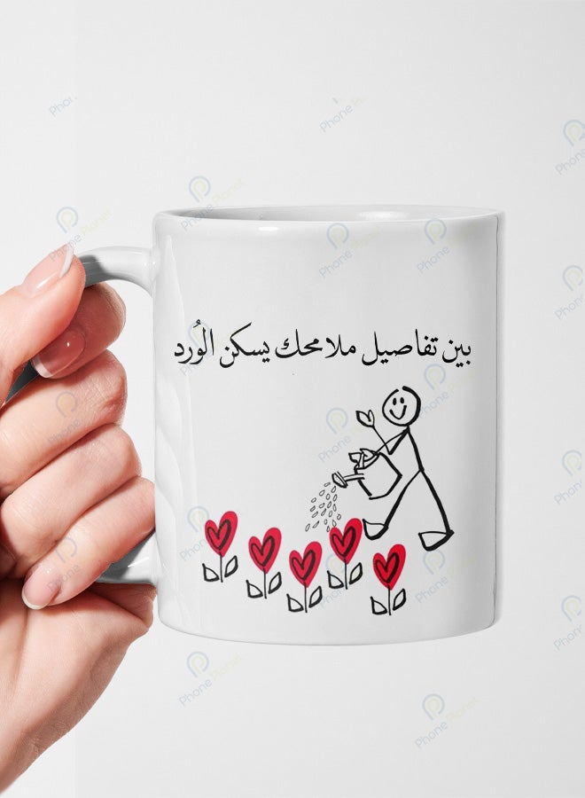 كوب من السيراميك مطبوع عليه عبارة بين تفاصيل ملامحك يسكن الورد ويتميز بمقبض مريح