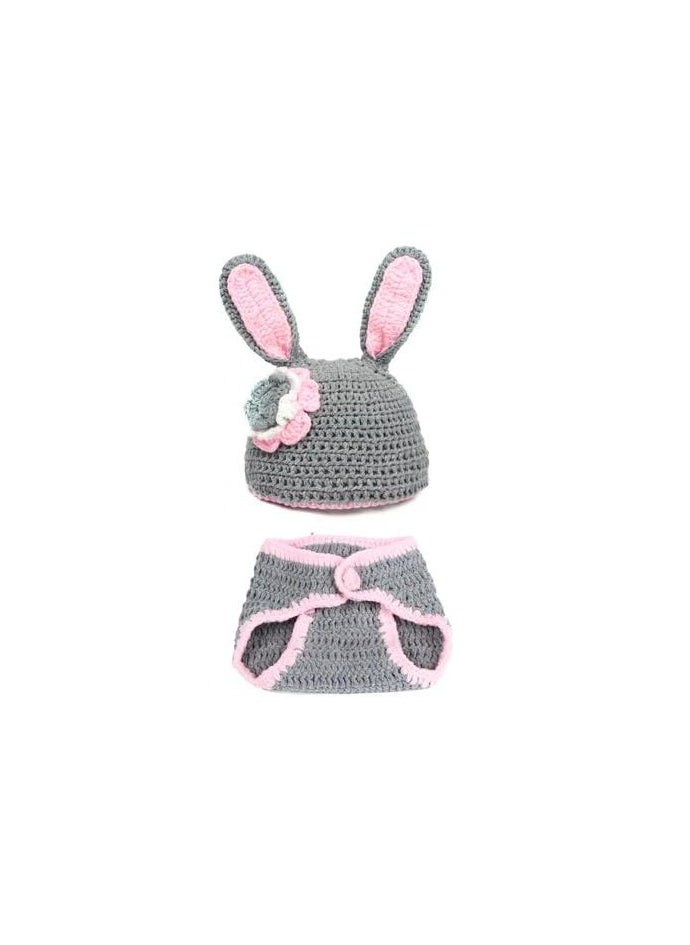 A crocheted baby boy consisting of a small hat with a bunny ears design decorated with a prominent rose, in addition to another piece used as a cover or comfortable clothing that is closed with buttons. The basic color of the set is light gray with pink edges, giving it an elegant and soft look suitable for children.