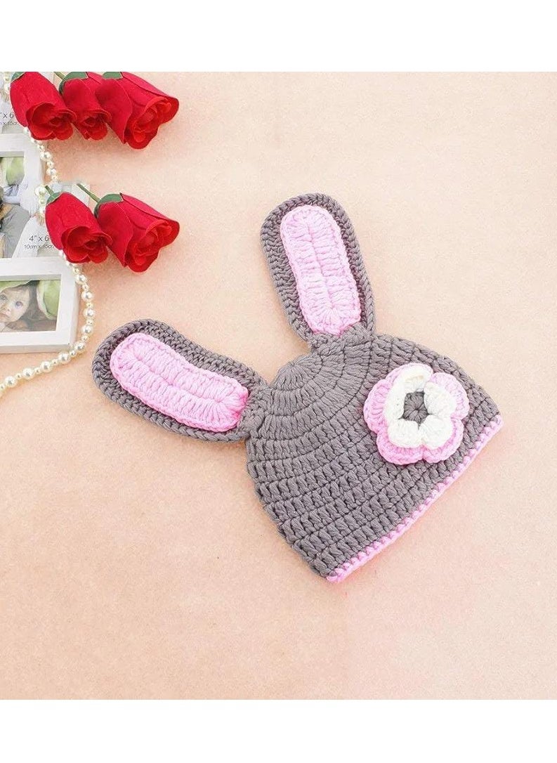 A crocheted baby boy consisting of a small hat with a bunny ears design decorated with a prominent rose, in addition to another piece used as a cover or comfortable clothing that is closed with buttons. The basic color of the set is light gray with pink edges, giving it an elegant and soft look suitable for children.