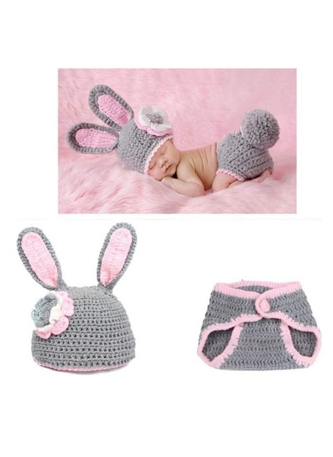 A crocheted baby boy consisting of a small hat with a bunny ears design decorated with a prominent rose, in addition to another piece used as a cover or comfortable clothing that is closed with buttons. The basic color of the set is light gray with pink edges, giving it an elegant and soft look suitable for children.