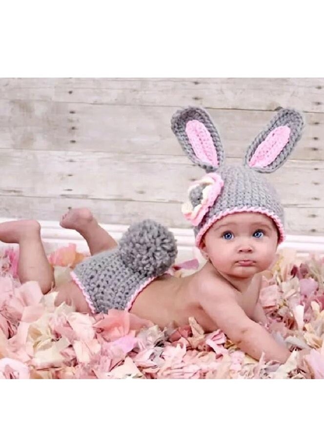 A crocheted baby boy consisting of a small hat with a bunny ears design decorated with a prominent rose, in addition to another piece used as a cover or comfortable clothing that is closed with buttons. The basic color of the set is light gray with pink edges, giving it an elegant and soft look suitable for children.