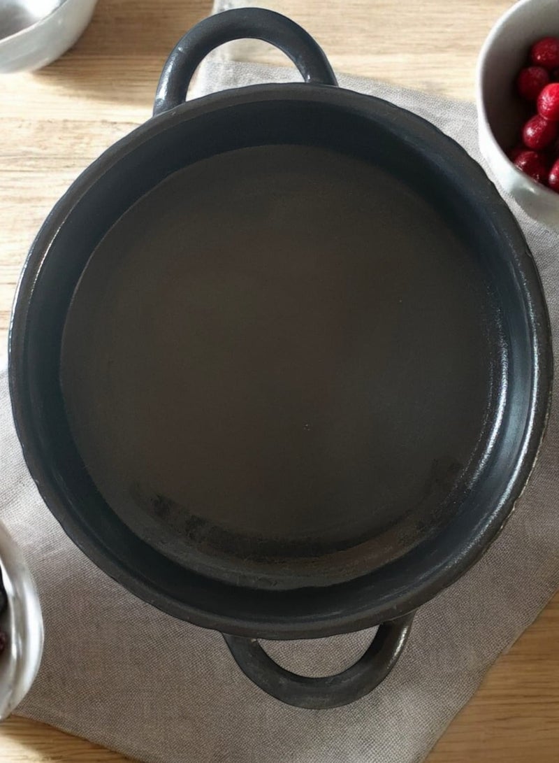 A 27cm black earthenware casserole dish that can withstand direct and indirect heat, suitable for use on a flame or in the oven. - Image 4