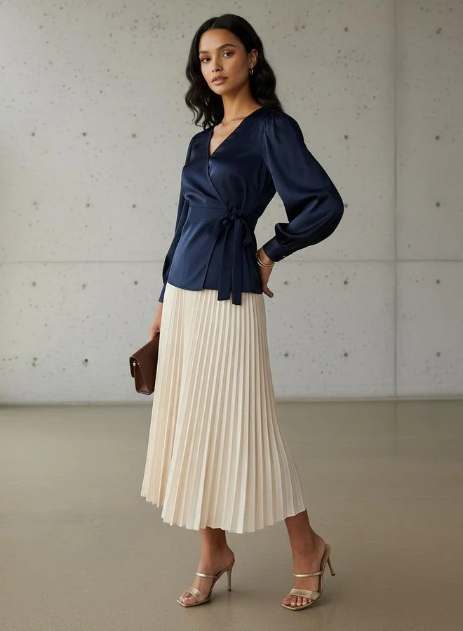 Woman in a navy wrap blouse with a pleated midi skirt