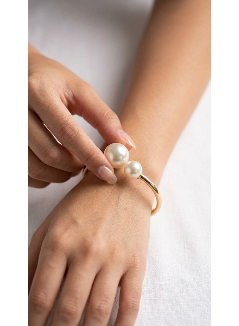 An elegant golden cuff bracelet adorned with two charming pearls of different sizes, adding a touch of classic delicacy and femininity to your wrist.