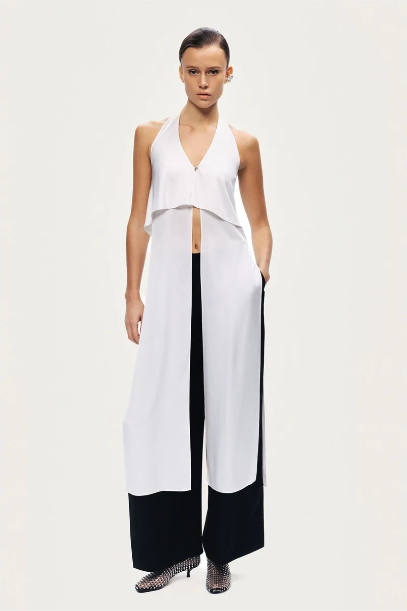 نوكتورن A sleek halter blouse featuring a layered front panel and an open-back silhouette. Designed with clean lines and fluid movement for a modern, elevated look.-True to size-Halter neckline with open back-Layered front detail-Lightweight, fluid fabric-Model is 5'11" (180 cm) tall with a 32.5" bust, 24.5" waist, and 36" hips, wearing a size S