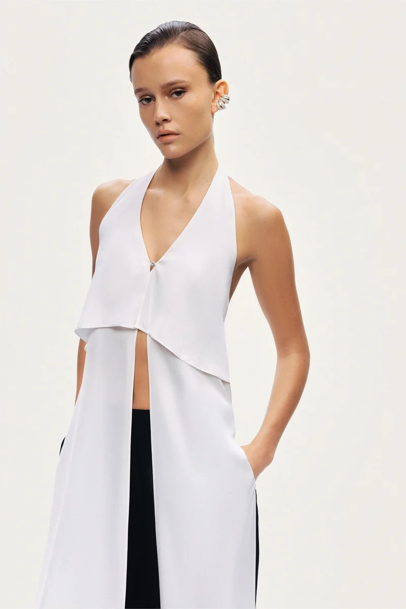 نوكتورن A sleek halter blouse featuring a layered front panel and an open-back silhouette. Designed with clean lines and fluid movement for a modern, elevated look.-True to size-Halter neckline with open back-Layered front detail-Lightweight, fluid fabric-Model is 5'11" (180 cm) tall with a 32.5" bust, 24.5" waist, and 36" hips, wearing a size S