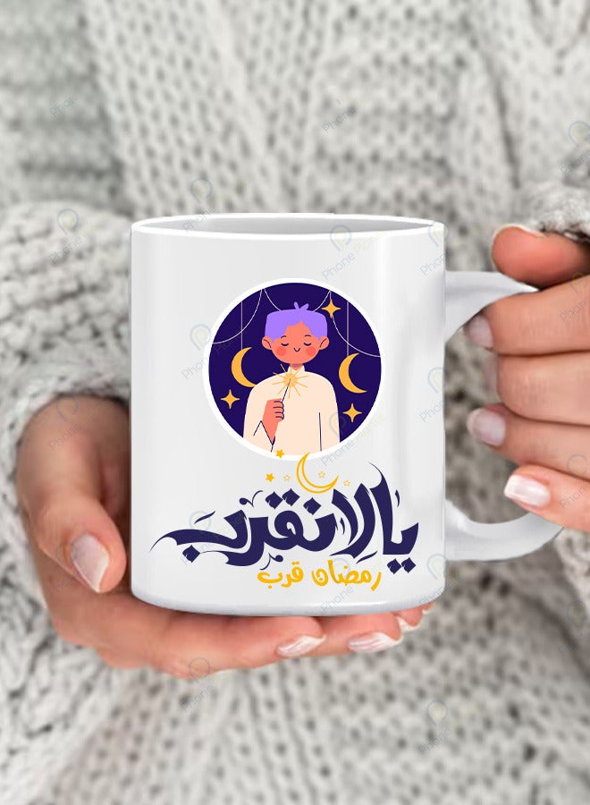 A mug printed with the phrase Let’s bring Ramadan closer with a multicolored handle A ceramic mug with a distinctive print