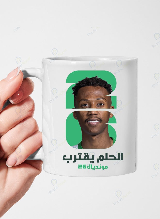 كوب من السيراميك الأبيض يحمل تصميمًا لنجم المنتخب السعودي ناصرالدوسري مع عبارة الحلم يقترب ومونديال 2026