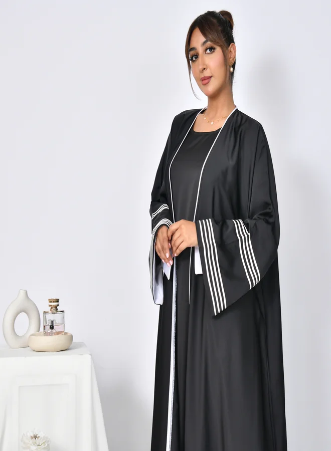 HAWRAA ABAYA Black abaya with wide sleeves decorated with white ribbons